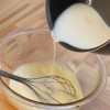 Passo 6: Despeje, aos poucos, o leite fervido na mistura mexendo constantemente para evitar que os ovos coagulem. Adicione a essência de baunilha.